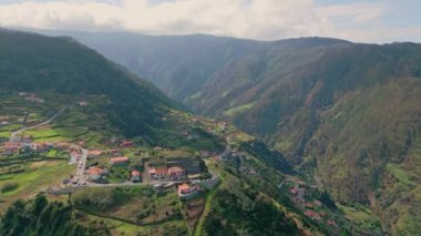 Dağ köyü yaz gezisi havadan görünüyor. İnsansız hava aracı, yuvarlanan tepeleri olan yeşil dağlar. Huzurlu Madeira vadisi ve manzaralı bir ortam. Gün ışığında küçük, huzurlu evler.