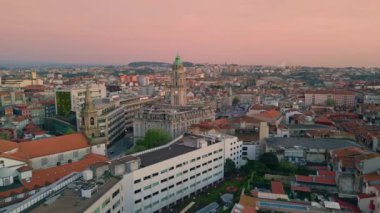 Güzel çatı, hava manzarası. Gün batımının canlı renkleriyle huzurlu şehir manzarası. Portekiz 'in geleneksel kırmızı kiremitli mahallesi. Pembe bir akşamda şehir mimarisinin ortasında seçkin bir saat kulesi.