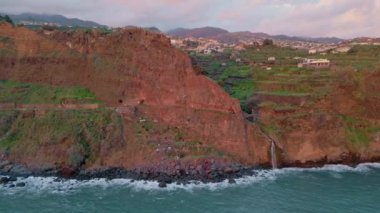 Güzel bir günbatımı adası uçurum manzarası. Altın güneş ışığında el değmemiş sakin bir doğa. Sabah havasında inanılmaz Madeira Adası 'ndaki deniz kenarındaki evler. Sakin okyanus yıkama resimli kayalık kıyı şeridi.