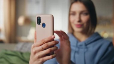 Oturma odasındaki akıllı telefondan video blogu kaydeden kız blogcu. Cep telefonu web kamerasına el sallayan gülümseyen kadın görüntülü aramaya başlıyor. Neşeli bayanın cep telefonuyla çevrimiçi toplantısı var.