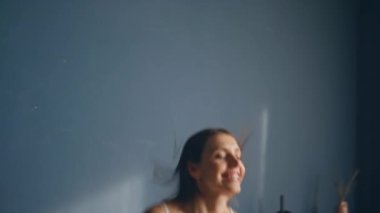 Gülümseyen bayan yatak odasına atlayıp hafta sonunun keyfini çıkarıyor. Beyaz pijamalı neşeli esmer daire yatağında tek başına eğleniyor. Mutlu kadın sabah heyecanı yaşıyor. Gülümseyen kız zıplıyor.