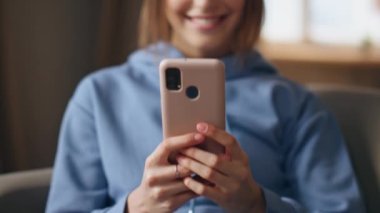 Oturma odasında cep telefonu tutan neşeli kadın elleri yakın plan. Hafta sonu evde cep telefonuyla oyun oynayan gülümseyen kız. Mutlu bayan uzaktan haberleşmenin, akıllı telefonun keyfini çıkar..