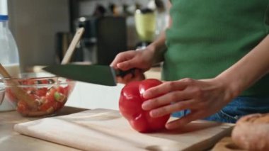 Kadın elleri mutfak tezgahında biber doğruyor. Yakın plan. Meçhul, yeşil bluzlu kadın modern mutfakta taze vitamin salatası hazırlıyor. Elinde bıçakla evde sebze pişiren genç bir kız..