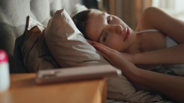 Uyanan kız cep telefonunu alıyor ve sabahın erken saatlerinde eve yakın çekim yapıyor. Yatak yastıklarına uzanmış rahat kadın gülümseyerek akıllı telefona bakıyor. Sakin esmer kız, yatak odasında sakince uyanıyor.