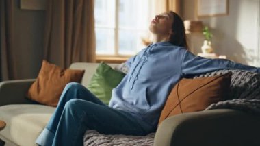 Yorgun bir kadın kanepede rahat bir şekilde oturur ve stres hisseder. Mavi kapüşonlu, rahat koltuğa düşen yorgun bir kadın sorunlarla boğuşuyor. Stresli kız baş ağrısı çeken kafaya dokunuyor..