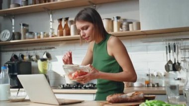 Freelancer mutfakta çalışıyor ve evde taze salata yiyor. Ciddi bir kadın vitamin sebzeleri çiğnerken dizüstü bilgisayara bakıyor. İş kadını çoklu görev güne sağlıklı bir kahvaltıyla başlıyor..
