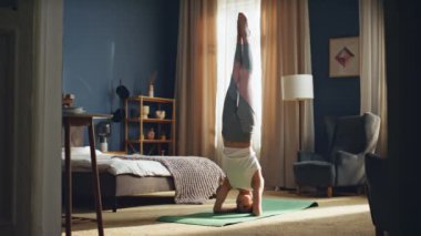 Evde yoga antrenmanında dengede duran sporcu kadın. Apartmandaki günlük eğitimde amuda kalkmış poz veren güçlü bir kadın. Atletik kız oturma odasında denge ve güç gösterisi yapıyor. Vücut germe.