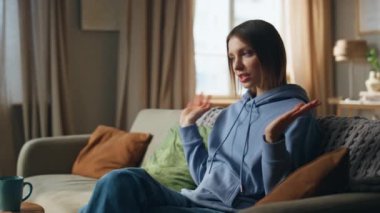 İnternetten konuşan bir kadın dizüstü bilgisayarın başında rahat bir daire kanepesinde oturuyor. Gülümseyen genç bayanın bilgisayar kamerasına işaret eden bir video görüşmesi var. Mutlu bayan internet sohbetinin tadını çıkarın..