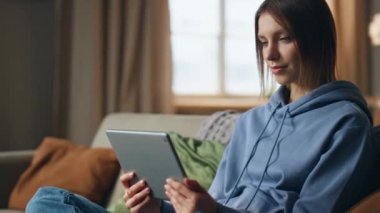 Tablet okuyan kız öğrenci oturma odasındaki kanepeye yakın çekim yapıyor. Evdeki bilgisayardan sosyal medyayı izleyen gülümseyen bir kadın. Rahat kadın serbest çalışan internet sitesi dijital aygıtı.