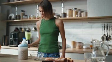 Modern mutfakta mısır gevreği hazırlayan kadın. Çağdaş mutfakta gevrek bir bayan taze sütü granola ile kaseye dolduruyor. Çekici kız düzenli bir evde kahvaltı hazırlıyor. Diyet kavramı