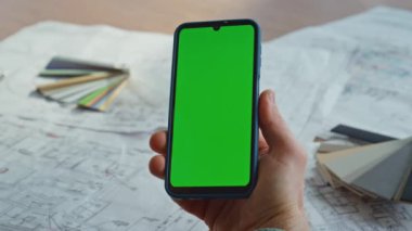 Mimarlık bürosunun iş yerinde yeşil ekran akıllı telefonu elinde tutan müdür. Bilinmeyen işadamı ofisteki model cep telefonunda arama uygulaması. Krom tuşlu cep telefonunu izleyen adam..