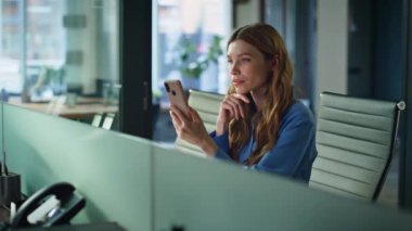 Ofis masasında akıllı telefon uyarısı okuyan odaklanmış bir iş kadını. Modern işyerinde cep telefonu ekranı arayan profesyonel yönetici. İş kadını cep telefonu uygulamasına bakıyor.