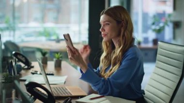 Modern iş yerinin iç kısımlarında ciddi bir cep telefonu ekranı var. Ofis masasında akıllı telefon uygulamasına odaklanmış iş kadını. İçerde sosyal medya içeriğini izleyen kadın yönetici