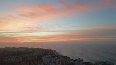 Güneşin doğuşu güzel kıyı şeridi hava manzarasına yerleştirilmiş kasabayı aydınlattı. Muhteşem turuncu gökyüzü güzel okyanusun üzerinde. Deniz suyu, sahil kentini çok yavaş çekimde yıkıyor. Alacakaranlıkta turuncu ufuk rahat tatil beldesinin üzerinde.