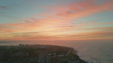 Tatil köyü üzerinde gün batımı ufku inanılmaz bir rıhtıma kurulmuştu. Alacakaranlıktaki güzel sahil kasabasının üzerinde parlak altın gökyüzü. Resimli karanlık okyanus kıyıları çok yavaş çekimde yıkıyor. Gün doğumu deniz manzarası.