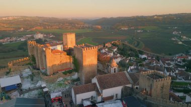 Ortaçağ şatosunda güzel köy hava manzarasında manzaralı bir akşam. Obidos 'un taş gibi antik duvarları gün batımında eski şehrin üzerinde yükseliyor. Resimli turist yerleşim yerinin üzerinde sabah ışığı.