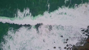 Beyaz okyanus köpüğü taştan sahil manzarasına doğru yuvarlanıyor. Dramatik deniz suyu çok yavaş çekimde güzel sahil şeridinde fokurduyor. Fırtınalı dalgalar sert kıyıları vuruyor. Doğal bir düzen oluşturuyor..