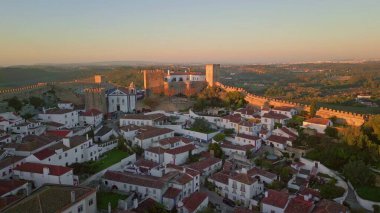 Obidos kalesi ve kırmızı kiremitli köy evleri üzerinde hava manzaralı gün batımı. Ortaçağ duvarları ve alacakaranlıkla yıkanmış rahat bir köy. Resimli alacakaranlık antik mimariyi geliştiriyor. Ünlü turizm beldesi.