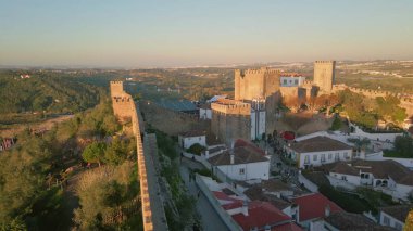 Drone gün batımında ortaçağ köyünün altındaki taş takviye duvarlarını vurdu. Antik tarihi mimari, manzaralı yeşil manzarayla harmanlanmış. Kırmızı kiremitli çatı binaları boyunca uzanan ölüm ilanları kalesi.