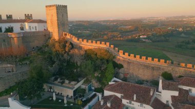 Günbatımı aydınlatma şatosu taş kuleleri eski köy insansız hava aracı manzarası üzerinde yükseliyor. Ortaçağ duvarlarını aydınlatan altın ışık ünlü turistik mekan. Antik tahkimat ve kırsal alanda sakin bir hava hakimdir..