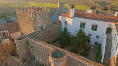 Küçük kasaba insansız hava aracı manzarası üzerinde devasa taş bir kale. Ortaçağ duvarları, köyün kırmızı çatılarına kadar uzanıyor. Güzel kuleleri olan tarihi mimari manzaralı şehir manzarası yaratır.