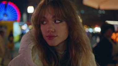 Eğlence parkında gülümseyen kadın yakın çekim ışıklarının keyfini çıkarıyor. Dönme dolap fuarının önünde duran portredeki kadın. Mutlu kız gece kameraya bakıyor Noel pazarında tatilde.