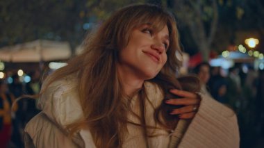 Şenlikli ışıklarda gülümseyen kadın kış gecesi pazarında dans ediyor. Neşeli bir kadın Noel meydanında eğleniyor, neşe içinde. Neşeli kız kameraya bakıyor Aydınlatılmış sokak fuarının tadını çıkarıyor.