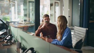 Ofis masasında kahve molası veren iki profesyonel. Neşeli kadın, erkek iş arkadaşıyla konuşuyor. Modern iç mekanlarda içecek servisi yapıyorlar. İş arkadaşları iş yerinde haberleri paylaştılar.