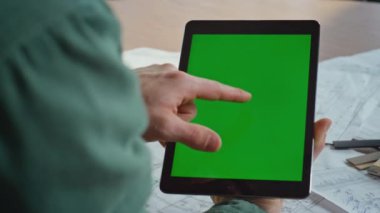 Proje yöneticisi ofisteki mimari planlar üzerinde çalışan yeşil ekran tabletine dokunuyor. Bilinmeyen serbest çalışan elleri krom anahtar pedi bilgisayarını tutuyor. Model aygıtından online alışveriş yapan adam.