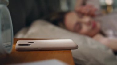 Bulanık, rahat bir yatakta uyuyan, gün ışığını aydınlatan bir kadın. Uykucu kız akıllı telefonuyla güneşli bir sabahta çalar saati kapatıyor. Çekici genç bayan rahat yastık odasında yatıyor. 