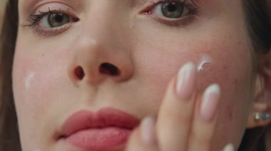 Makro genç kadın kozmetik krem sürüyor. Banyo manzarasında model temizleme suratı. Rahatlamış model bayan nemlendirici cilt bakım losyonu kameranın yakın plan portresine bakıyor. Cilt bakımı sağlık konsepti