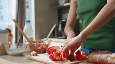 Kadın elleri sebzeleri dilimliyor. Mutfakta kablosuz kulaklıkla müzik dinliyor. Mutfakta kırmızı biberli taze salata hazırlayan mutlu kadın. Kulaklıklı neşeli kız yemek yapmayı seviyor.