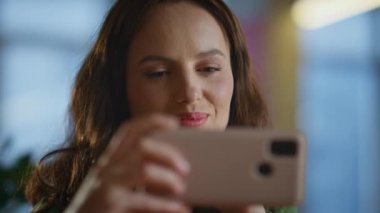 Ofiste gülümseyen kadın cep telefonunu yakından görüyor. Akıllı telefondan e-posta okuyan neşeli iş kadını. Patroniçenin elinde cep telefonu var. Modern odanın içinde Webinar 'ın tadını çıkarıyor.