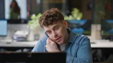 Şirket çalışanı telefonla konuşuyor. Bilgisayarla yakın çekimde çalışıyor. Modern ofiste monitörle akıllı telefondan konuşan başarılı traşsız iş adamı. İş yerinde cep telefonu bulundurmakla meşgul. 