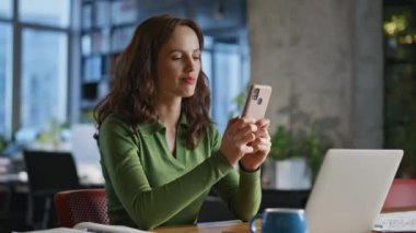 Bayan yönetici cep telefonunu yakın çekimde tutuyor. Laptop masasında çalışan gülümseyen genç iş kadını modern yaratıcı ofiste fikirler düşünüyor. Kabinede akıllı telefon yazan şirket çalışanı dinleniyor.