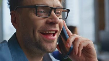Şirket işyerinde cep telefonundan konuşan yakın plan iş adamı. Gülümseyen adam akıllı telefondan arıyor iş anlaşmasını uzaktan tartışıyor. Ofiste klavye yazan cep telefonu konuşan yakışıklı girişimci. 