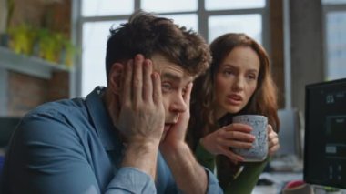Endişeli iş çifti kahve içerken yakın planda konuşuyor. Üzgün şirket çalışanları bilgisayar monitörü görünümlü bej dolapta cappuccino ile ofiste oturuyorlar. İş arkadaşları üzgün hisseder