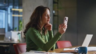 Rahat iş kadını cep telefonuna bakıyor. Laptop 'taki iş yerindeki mesajları okuyor. Yakın plan. Ofiste cep telefonu cevap veren bir yönetici. Pozitif patron akıllı telefon ekranına dikkatlice bakıyor.