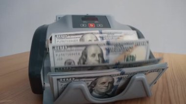 Kapalı mekanda dolar sayan makineler. Banka finansal işlemleri için otomatik ekipman. Masada 100 doların döviz değişimi var. Yatırım sermaye işlemleri kavramı