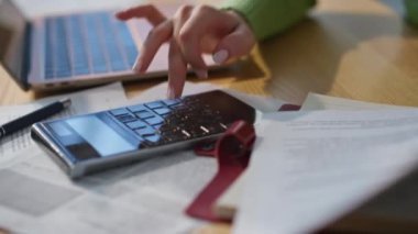 Kadın, hafif iş yerindeki el hesaplama bütçesini kapatıyor. Tanımlanamayan bayan yönetici modern evde hesap makinesi tuşlarına basarak şirket giderlerini hesaplıyor. Ahşap masada çalışan tanınmamış bir iş kadını.