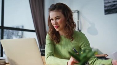 Kadın yönetici ofiste sanal konferans konuşması yapıyor. Gülümseyen yönetici konuşuyor. Panoramik pencere odasındaki bilgisayar bilgisayarını ara. Neşeli bayan internette iyi haberleri dinlemekten zevk alıyor. 
