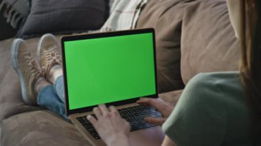Freelancer ev kanepesinde otururken dizüstü bilgisayar uygulamasını tarıyor. Apartman kanepesinde yeşil ekranda yazan kimliği belirsiz kadın. Uzaktan kumanda yöneticisi kapalı alanda krom anahtar dijital aygıt üzerinde çalışıyor.