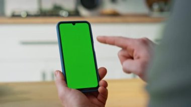 Akıllı telefon yeşil ekran çevrimiçi tarama uygulaması daire kapanışında. Modern evde elinde krom anahtarlı cep telefonu olan tanınmayan bir iş adamı. Model etkileşimi için boş ekran.