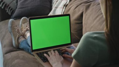 Yeşil ekranlı dizüstü bilgisayarı rahat kanepeye yakın çekim yapan bir kadın. Bilinmeyen kadın serbest yazar klavye model bilgisayarına iş e-postası yazıyor. Uzaktan kumandalı koltukta çalışan genç bayan programcı..