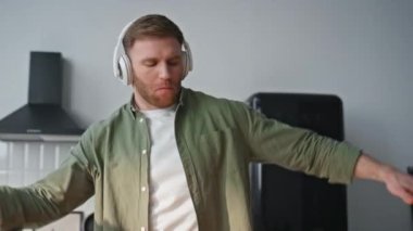 Daire mutfağında kahvaltı hazırlayan dansçı adam kulaklık takıyor. Ev mutfağında kablosuz kulaklıkla müzik dinleyen komik adam. Kaygısız erkek ev yemeği hazırlarken eğleniyor.