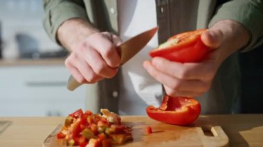 Erkek eli, ahşap pano ev mutfağında salata için sebze malzemesi hazırlıyor. Bilinmeyen adam mutfakta kırmızı biberi bıçakla kesiyor. Erkek aşçı kahvaltıda sağlıklı organik yemek yapıyor..