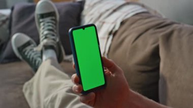 Parmak kaydırmalı akıllı telefon kanepe evinde dinleniyor. Yakın plan. Kanepedeki yeşil ekranda internette sörf yapan tanınmamış genç bir erkek. Krom anahtarlı cep telefonunda mesaj okuyan adam.