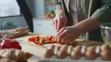 Adam, modern mutfakta vejetaryen salatası için sebze hazırlıyor. Kablosuz kulaklıkla müzik dinleyen rahat adam ev mutfağında yemek pişiriyor. Tezgahta kırmızı biber dilimleyen mutlu erkek..