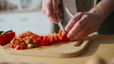 Bilinmeyen bir adam ev mutfağında sebze doğruyor. Adam taze kırmızı biberi bıçakla doğrayıp öğle yemeği hazırlıyor. Yemek meraklısı salata için sağlıklı vitamin malzemeleri hazırlıyor..