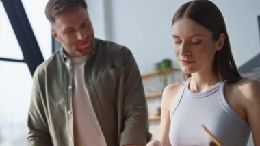 Modern mutfakta birlikte yemek pişiren harika bir çift. Mutlu adam ve kadın evde yemek hazırlarken kaynaşıyorlar. Sevgili koca, gülümseyen eş gözlerini kapatıyor. Mutfakta ev işlerinin keyfini çıkarıyor..